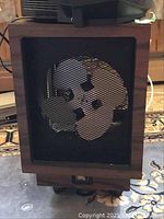 Front view of the wooden cabinet fan showing metal mesh covering the fan blades inside.