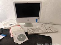 Apple iMac desktop computer with wired keyboard and multiple Mac OS installation discs on a table