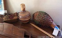 Photo showing entire lot arranged on wooden furniture including shekere, clay jar, wooden sticks, decorative pine cones in tray