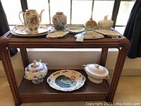 Wide view of the lot displayed on wooden shelf, showing porcelain vase, plates, platter, tureens, and teapot