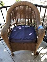 Full view of weather-worn brown wicker chair with square dark blue cushion on seat.