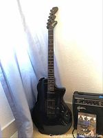 Full length view of black Esteban electric guitar standing upright beside Esteban amplifier