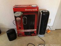 Photo showing the Honeywell radiator in original box alongside a Lasko tower heater and a smaller black portable heater on the floor.
