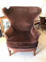Front view of vintage wingback chair in dark brown suede upholstery with brass tacks. Shows curved back and cushioned seat. Paint marks visible on upholstery.