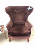 Front view of vintage wingback chair showing brown suede upholstery with brass tacks and carved wood legs.