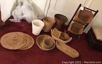 Multiple cane and wicker baskets arranged on carpeted floor, including white, dark brown, and natural wicker colors, also includes woven placemats/trivets.