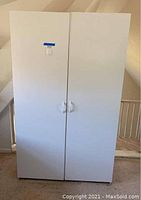 Front view showing two white doors with curved handles on the white storage closet cabinet