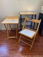Photo showing foldable wooden chair with white seat cushion and two small foldable wooden tables with light wood finish on hardwood floor.