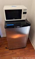 Front view of Haier portable refrigerator with RCA microwave placed on top showing stainless steel door with black trim and white microwave with control panel.