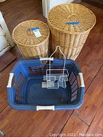 View of two wicker laundry baskets with lids, blue plastic laundry basket, and white metal hanging organizer on wooden floor.