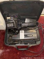 Quasar VHS film camera inside hard plastic case with battery and charger cords visible