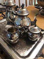 Photo showing entire set on table including tea pot, coffee pot, creamer, sugar bowl, and tray with detailed floral embossing.