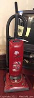 Full view of red Dirt Devil Jaguar upright vacuum cleaner with handle and hose standing upright in front of furniture