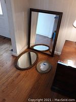 Three mirrors placed on the floor showing different shapes and sizes, including one large rectangular, one oval, and one smaller round mirror.