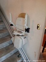 Stairlift chair mounted on track along carpeted stairs, showing armrests and footrest