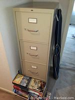 Front view of the beige HON metal 4 drawer file cabinet with portable projector screen case leaning next to it.