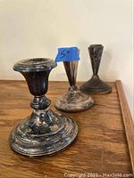 Photo showing three tarnished weighted sterling silver candle holders by Frank M. Whiting, arranged on wooden surface, with visible wear and oxidation.