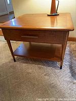 Front view of wood side table showing single drawer with metal handle and bottom shelf