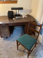 Overall view of wood desk with laminated top featuring dovetailed drawers, showing contents on top not included and scratches, along with wood chair with cushion seat.