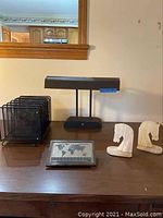 Photo showing black metal desk lamp, black metal mesh file holder, horse head marble-look bookends, and Seiko world time voice alarm clock on wood surface.