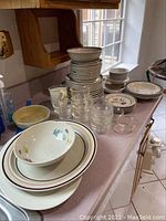 Overall lot showing stacked Pfaltzgraff dishes including plates, bowls, clear glass bakeware, and Franciscan bowl arranged on kitchen counter