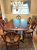Photo of antique wooden dining table with six matching chairs around it in a dining room, showing table surface and chair backs