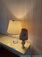 Set of two lamps on a shelf, one glass with brass base and one small ceramic with small shade showing staining