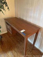 Full view of wooden desk showing top surface and legs against wall on hardwood floor.
