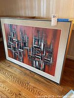 Front view of framed abstract painting with red background, black and white geometric pattern in wood frame.