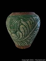 Front view of large terracotta planter showing carved Monstera leaf pattern with green coloring on a natural terra cotta background.