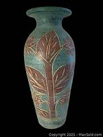 Full front view of the tall terracotta planter showing teal glaze and large carved flower and leaf design in reddish brown.