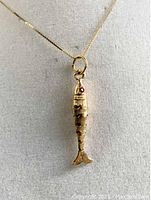 Close-up of fish pendant hanging on chain showing scales and red gemstone eye