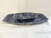 Side view of two rectangular blue speckle Bennington Pottery platters stacked, larger below smaller