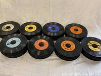 Stacks of vintage 45 RPM rock and roll vinyl records with various colored labels including white, yellow, blue, orange and black.