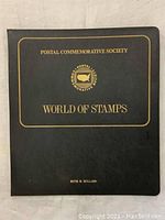 Front cover of black binder with gold text 'Postal Commemorative Society World of Stamps'.