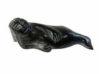 Front view of polished dark soapstone carving depicting a reclining seal woman