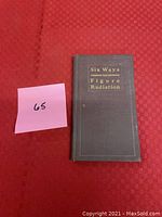Closed front cover of the book titled "Six Ways to Figure Radiation" with a small pink sticky note numbered 65.