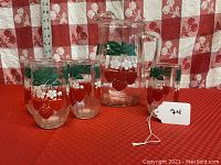 Pitcher and 5 tumblers arranged on red checkered surface showing front view of their strawberry and leaf pattern