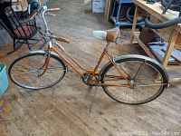 Side view of the vintage Schwinn Deluxe Breeze bicycle showing the orange frame, white and brown saddle, fenders, and handlebars.