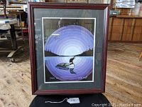 Frontal photo of the framed painting featuring the loon and circular evening sky design in purple hues.