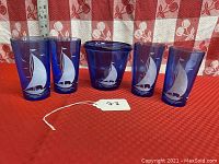 Set of 5 cobalt blue glass items with sailing ship motif, showing 4 tumblers and one ice bucket.