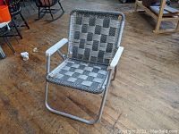 Aluminum folding lawn chair with white armrests and black and white woven macramé webbing seat and backrest. Slight bend visible on frame.