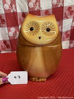 Front view of owl cookie jar showing brown gradient glaze and stylized eyes, tape residue visible.