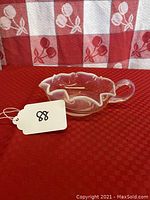 White opalescent glass olive nappy with ruffled edge and handle displayed on red plaid fabric.