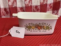 Oblong white CorningWare casserole dish with colorful vegetable design and small handles on each side, set on a red checkered background
