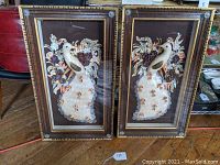 Full view of both framed seashell bird shadowbox artworks showing the pair as matching pieces with intricate shell detailing and wood frames.