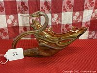 Photo showing large art glass swan bowl with amber swirls and opaque white accents on a red and white patterned background.