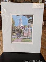 Photo of the limited edition print by Robert E. Kennedy wrapped in plastic with white matting, showing a colorful street scene with buildings and trees.