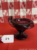 Side view of the amethyst art glass jack in the pulpit vase on a red patterned cloth background.