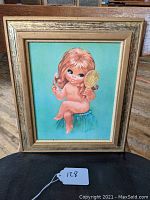 Full view of framed mid-century big eyes framed print artwork by W.M. Otto showing child sitting on blue cushion with turquoise background